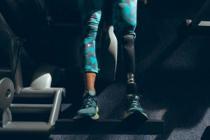 Low section of disabled active senior Caucasian woman with leg amputee exercising with leg press machine in fitness studio. Strong active senior female amputee training and working out